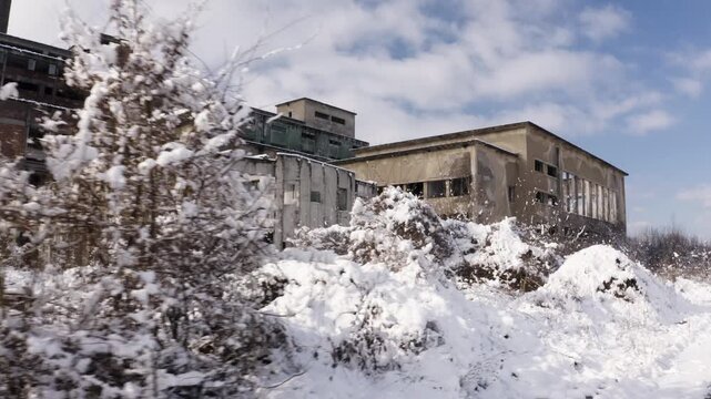 Large abandoned factory covered in snow during winter. Broken windows deteriorating walls neglected vegetation decaying industrial architecture urban decay deindustrialization economic decline 