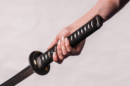 A samurai katana sword being held by a woman, close up on sword handle and hands