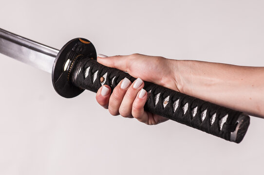 A samurai katana sword being held by a woman, close up on sword handle and hands