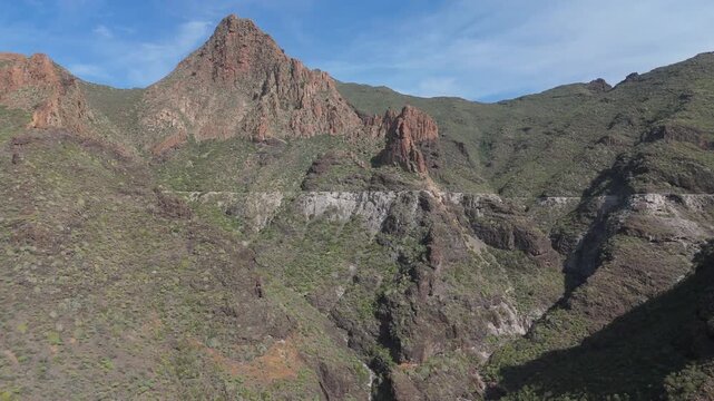 Boom up aerial drone shot revealing the dramatic, rocky landscape of Tenerife. The majestic mountain Risco Blanco and deep valleys are covered with sparse vegetation.
