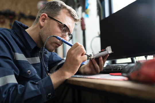 Male electrician engineer using soldering iron repairing electronic printed circuit board. Electrician checking, maintenance connecting electronic components on operation electric system