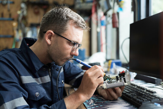 Male electrician engineer using soldering iron repairing electronic printed circuit board. Electrician checking, maintenance connecting electronic components on operation electric system