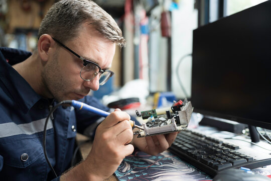 Male electrician engineer using soldering iron repairing electronic printed circuit board. Electrician checking, maintenance connecting electronic components on operation electric system