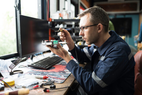 Male electrician engineer using soldering iron repairing electronic printed circuit board. Electrician checking, maintenance connecting electronic components on operation electric system