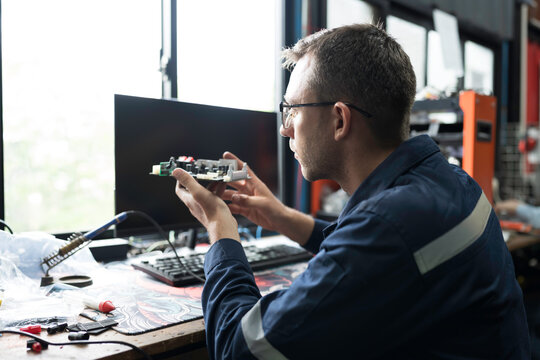 Male electrician engineer using soldering iron repairing electronic printed circuit board. Electrician checking, maintenance connecting electronic components on operation electric system