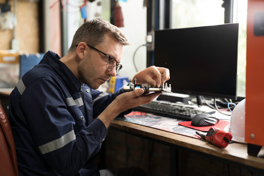 Male electrician engineer using soldering iron repairing electronic printed circuit board. Electrician checking, maintenance connecting electronic components on operation electric system