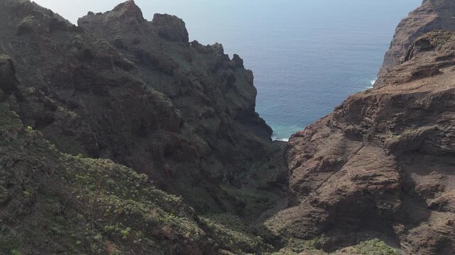Aerial drone shot showcasing rugged coastal cliffs and a deep valley on Tenerife. Drone pushes in and booms down, revealing the Playa de Barranco Seco and the neighbour island La Gomera.