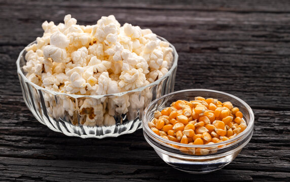 Close-up view of crunchy popcorn and dried corn kernels in glass bowls on a rustic wooden background.