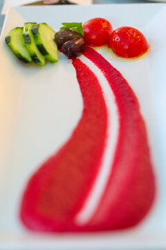 Artfully plated beet puree with cucumber slices, olives, and cherry tomatoes on a white dish, showcasing the vivid color and refined presentation of Mediterranean fine dining in Santorini.