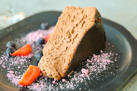 Slice of burnt cheesecake with chocolate mousse texture, garnished with strawberries, blueberries, and pink sugar dust, creating a rich and colorful dessert presentation.