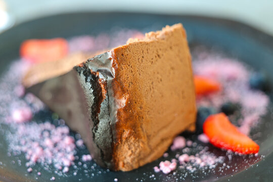 Slice of burnt cheesecake with chocolate mousse texture, garnished with strawberries, blueberries, and pink sugar dust for dessert.