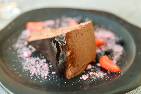 Slice of burnt cheesecake with chocolate mousse texture, garnished with strawberries, blueberries, and pink sugar dust for dessert.