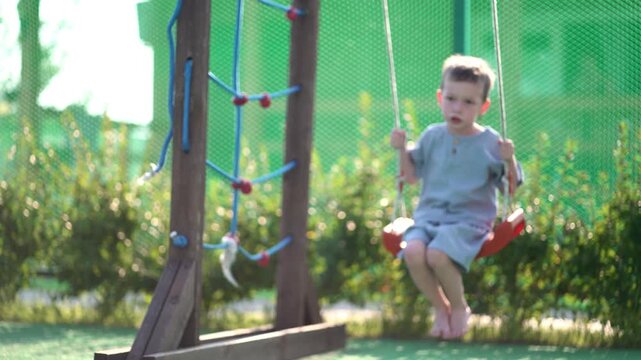 Happy young boy swinging with a big smile on a sunny playground. Carefree childhood joy captured in vibrant outdoor summer setting perfect for family, kids activities and lifestyle projects. Bright na