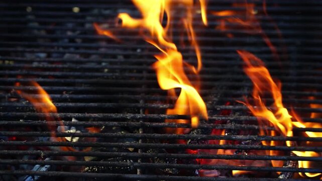 Glowing hot charcoal in barbecue grill pit with open flames close up background texture for bbq cooking and outdoor fire concept