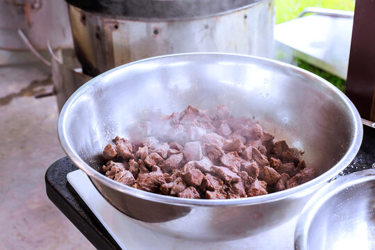 Small pieces of beef are being cooked in metal bowl over hot stove in an outdoor setting.