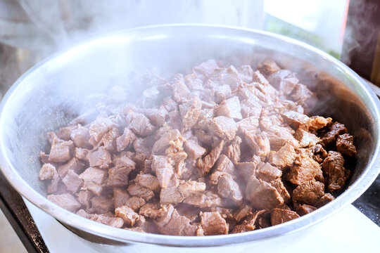 Beef is being cooked in large pot on stove, with steam rising in kitchen