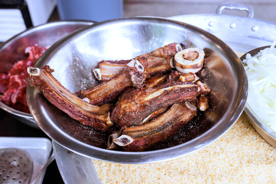 Bowl contains pieces of meat with bones, alongside rice other ingredients on countertop in kitchen.