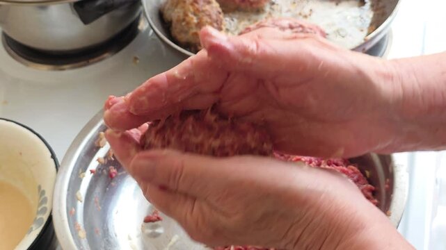 Elderly hands of a cook preparing raw minced meat patties, shaping beef cutlets for frying, showcasing a traditional home cooking recipe with ground pork and onion