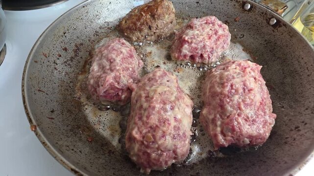 Homemade minced beef and pork meat cutlets sizzling in hot oil in a seasoned frying pan on a stove top, a traditional comfort food meal for dinner cooking concept