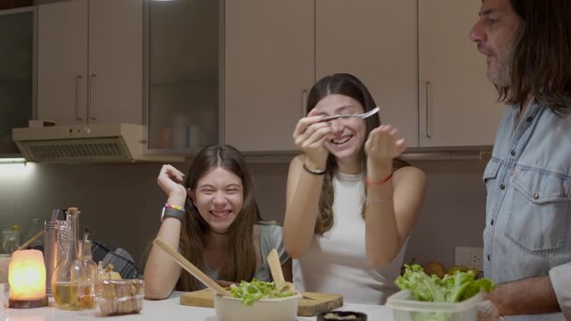 A modern family of a single father and two teenage daughters are having fun preparing a healthy salad for dinner.