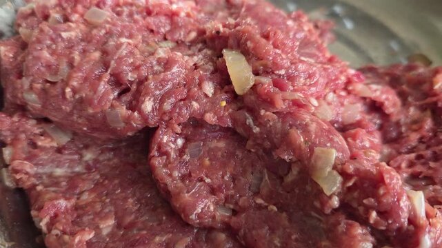 Raw ground beef meatball preparation with chopped onion and seasoning rotating in a metal bowl, a detailed view of the fresh red meat ready for cooking dinner