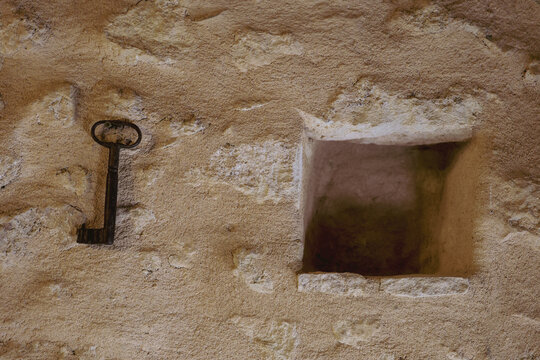 An antique iron key hangs on a textured stone wall beside a small recessed niche. The simple composition highlights traditional architecture and historic character in Crete, Greece.