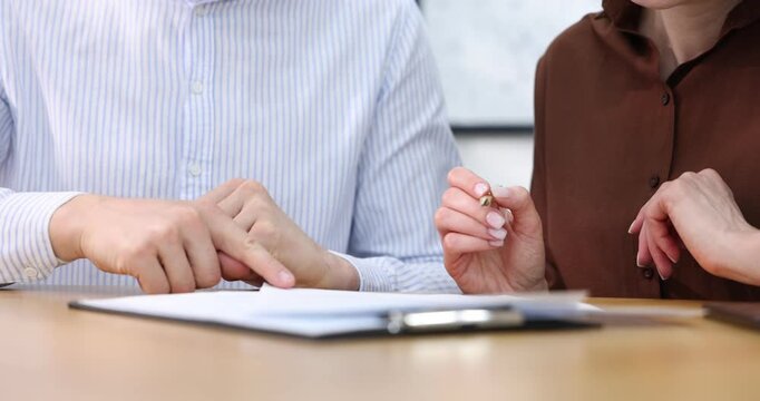 Insurance agent showing client where to sign document at table in office, closeup