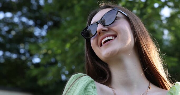 Beautiful young woman in stylish sunglasses outdoors, low angle view. Camera moving in