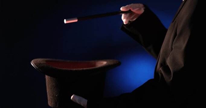 Magician showing trick with wand and top hat on stage, closeup