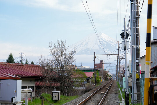 Railway Crossing and Train Tracks Leading toward Mount Fuji Snow Peak in Japan A scenic perspective along a railroad track with a level crossing barrier in a local Japanese town.