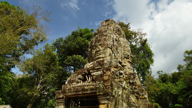 Ancient stone tower with giant carved face surrounded by green jungle