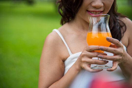 Beautiful women laydown picnic mat fruit basket hands holding healthy drinking glass. Asian Women picnic in green park smilng face hands holding glass of orange juice fresh fruit cool summer drinking