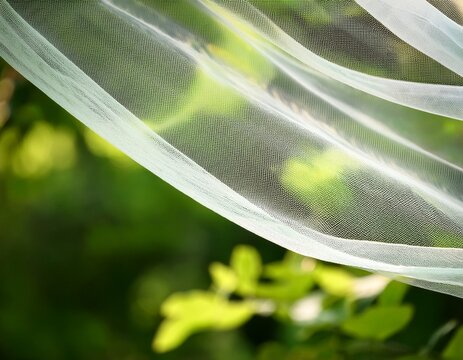 sheer textured fabric billows gently against a blurred backdrop of lush green foliage