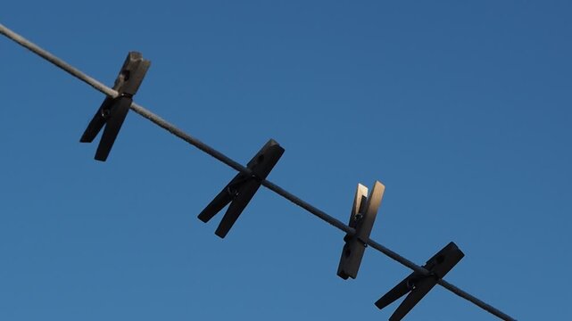 Hand clips laundry pin against clear blue sky. Action suggests care, routine, and simplicity