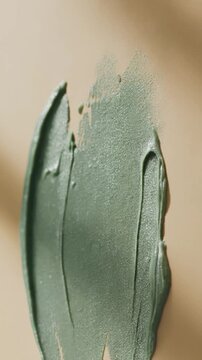 Botanical green clay mask vertical stroke with brush texture on a warm background.