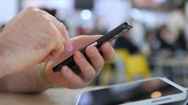 Close-up of hand holding smartphone. Fingers tap screen actively. Background shows blurred public space. Person appears focused and engaged. Ideal for digital communication or mobile usage concepts