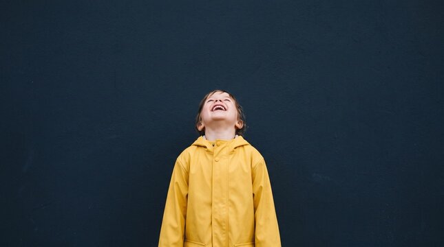 Joyful child in yellow raincoat laughing against dark blue background
