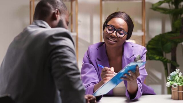 African businesswoman in glasses and purple blazer discussing documents with a male colleague in office