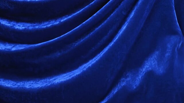 Velvet fabric displays deep blue folds and soft shadows that drape in a luxurious elegant pattern to provide a rich textural backdrop for creative commercial displays and professional studio.