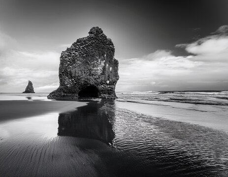 isolated rock formation standing on beach in black and white photo