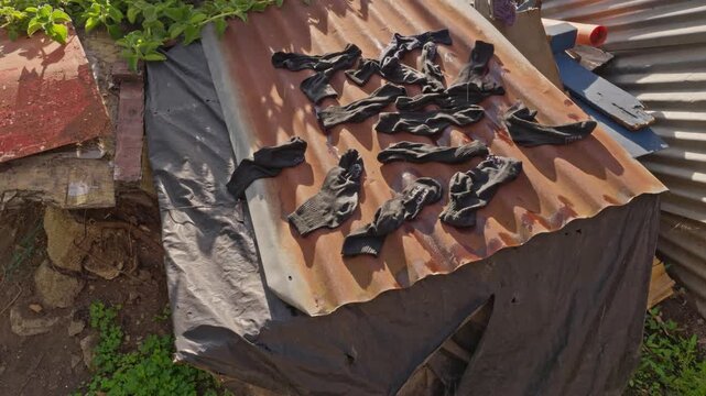 Dark clothing laid out to dry over a corrugated sheet metal structure installed above a black plastic covering in the outdoor area.