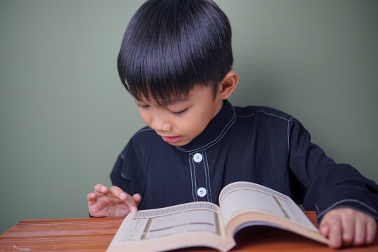 Young Muslim boy studying the Quran at home, representing Islamic education, religious learning, faith, and childhood spiritual development.