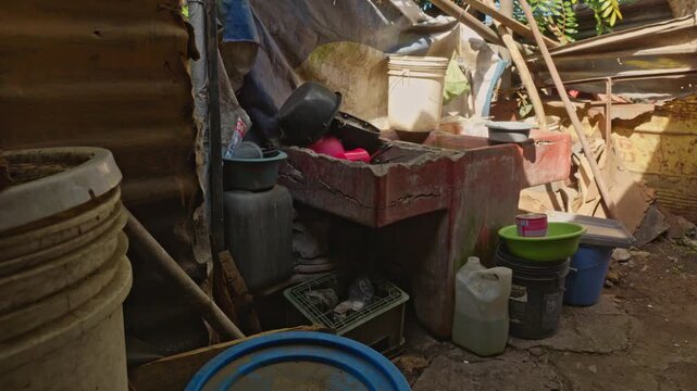 View of an outdoor washing area featuring a rustic concrete sink, surrounded by containers, buckets, and supplies under a makeshift structure.