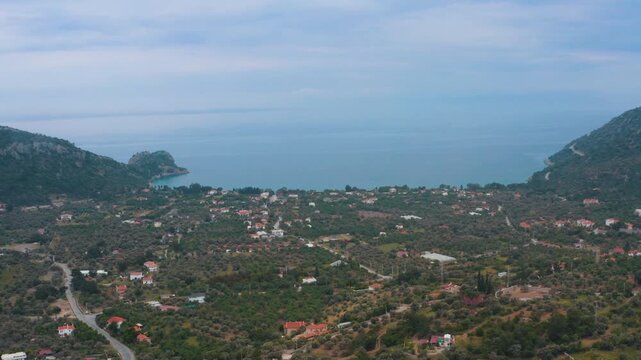 Cinematic wide-angle aerial drone shot of the peaceful coastal village and calm blue bay nestled among the lush green hills of Hayitbuku, Datca.