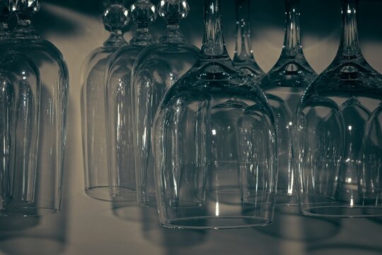 Macro close up shot of upside down crystal wine glasses hanging in a row with dark moody cinematic tones and reflections