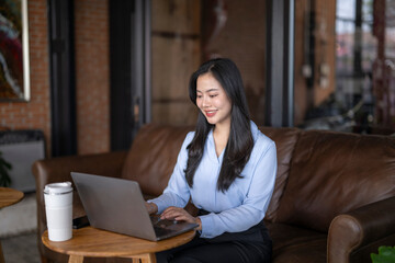 Fototapeta premium Young woman working on laptop in modern cafe with coffee cup