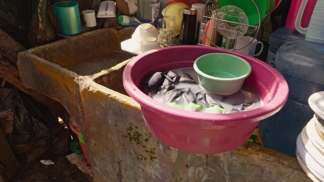 Framing centered on a pink tub with soapy water and dark garments soaking on the edge of an outdoor concrete sink.