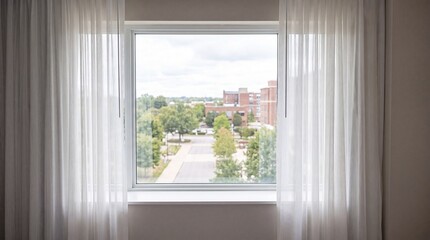 Obraz premium Window with sheer curtains overlooking a leafy city street with residential buildings