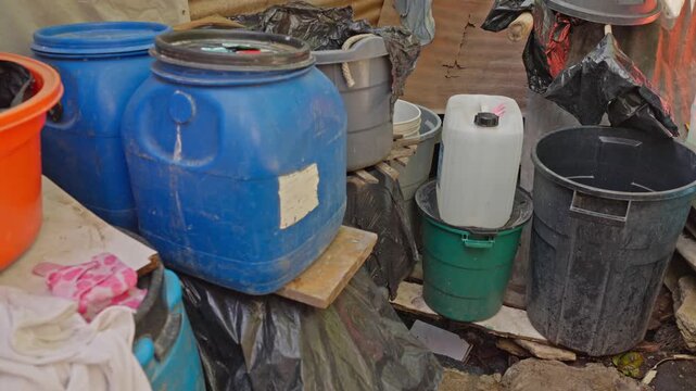 Accumulation of plastic containers, blue jugs, and buckets organized on informal supports in an outdoor utility area.