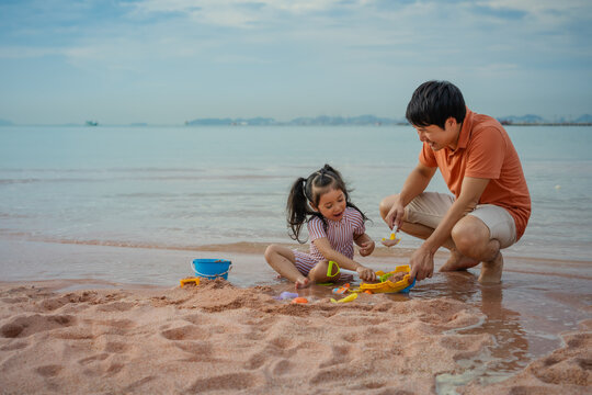 happy preschool child girl playing sand toy with father on the sea beach in Pattaya, Thailand